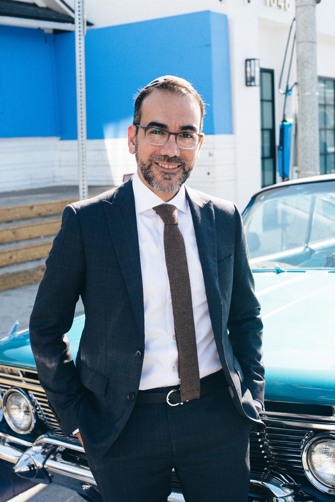 Rabbi Nissan portrait in navy suit, standing by a vintage teal car