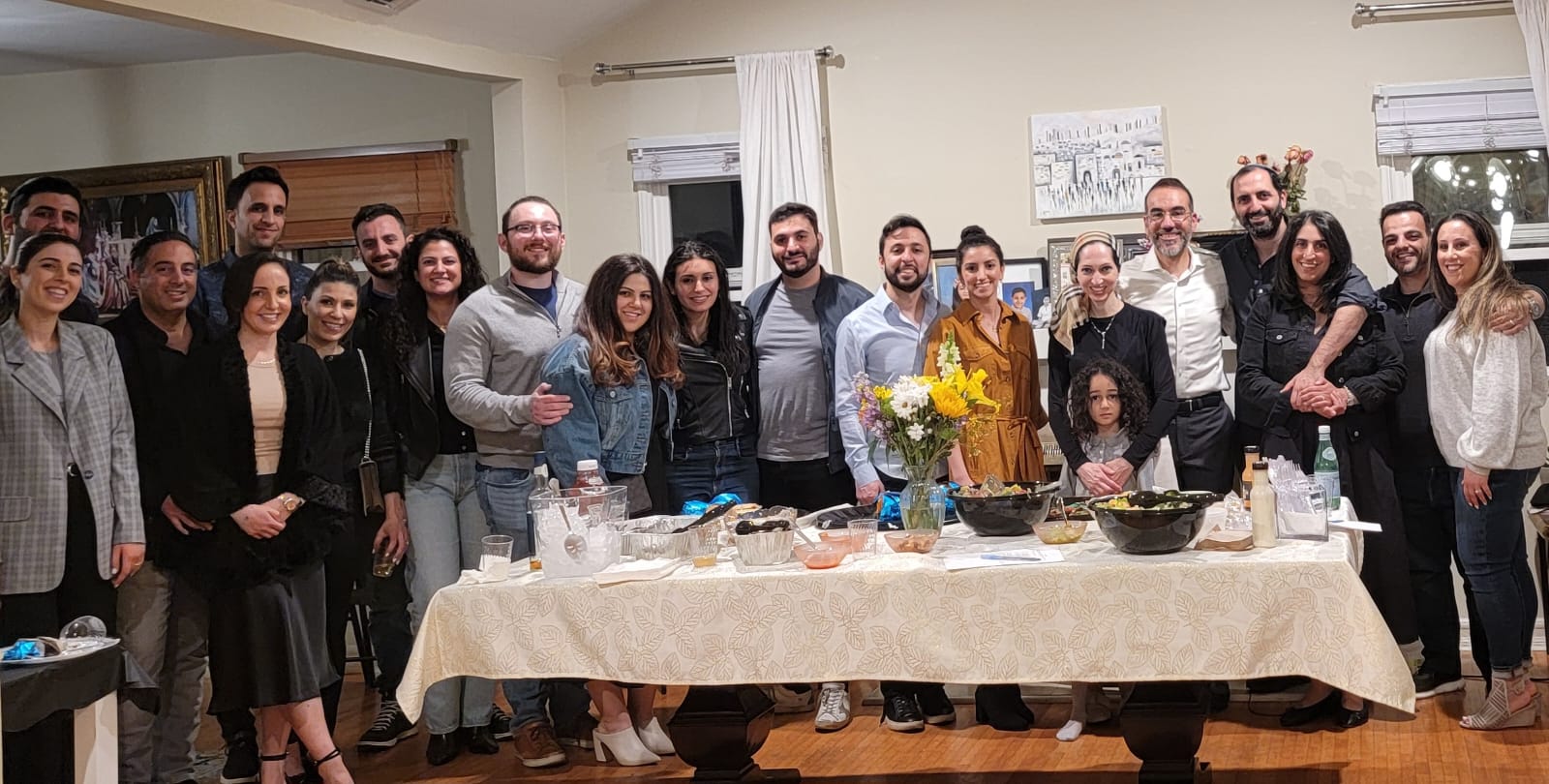 A community gathering in Rabbi Nissan's home — group portrait around a flower-topped table